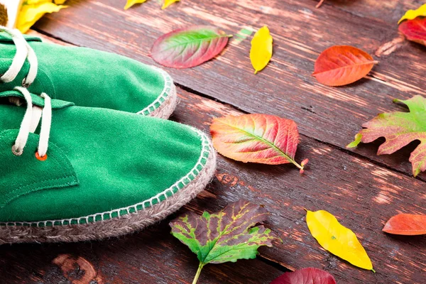 Green man suede boots espadrilles on wooden background with leaves. Autumn or winter shoes.Flat lay.