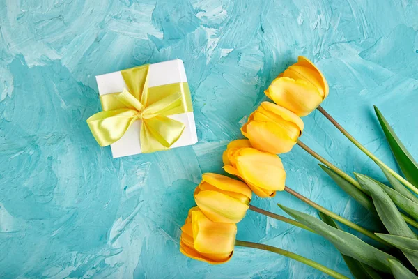 Białe Pudełko Żółtą Wstążkę Pobliżu Żółty Tulipan Niebieskim Tle Leżał — Zdjęcie stockowe