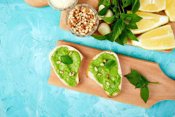 Bruschetta bread with pesto sauce, parmesan cheese and fresh basil leaves on blue background. Snacks. Antipasto. Crostini. Italian food. Top view. Flat lay. Copy space.