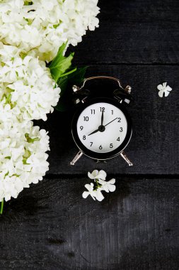 Siyah çalar saat ve siyah arka plan üzerine beyaz çiçekler. Anne ya da kadınlar günü. Tebrik kartı iyi sabah kahvaltı. Bahar. Romantik. Üstten görünüm. Uzay kopyalayın. Düz yatıyordu