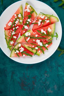 Taze yaz karpuz salatası beyaz peynir ve roka yeşil tablo arka plan üzerinde. Vegan gıda. Diyet, vejeteryan. Üstten görünüm. Düz yatıyordu. Kopya girintili