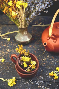 Bardak bitkisel çay - tutsan, adaçayı, kekik, helichrysum, lavanta yakınındaki koyu ahşap arka plan üzerinde kahverengi çaydanlık. Bitkisel çay. Kuru otlar ve çiçekler, bitkisel ilaç.