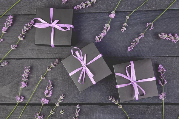 Black Gift box with violet ribbon and bouquet of flower lavender on black background. Celebration, birthday. Decoration present. Flat lay. Copy space.