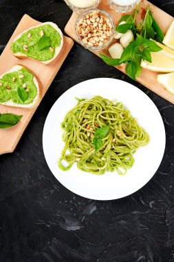 Koyu arka plan üzerinde kahvaltilari ile ev yapımı fesleğen pesto ile İtalyan makarna spagetti. Meze. Bruschetta pesto soslu. Sağlıklı gıda. İtalyan yemeği. Üstten görünüm. Uzay kopyalayın. Düz yatıyordu