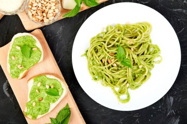 Koyu arka plan üzerinde kahvaltilari ile ev yapımı fesleğen pesto ile İtalyan makarna spagetti. Meze. Bruschetta pesto soslu. Sağlıklı gıda. İtalyan yemeği. Üstten görünüm. Uzay kopyalayın. Düz yatıyordu