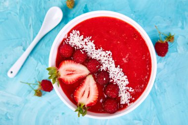 Güler yüzlü kase. Mavi arka plan üzerinde sağlıklı kahvaltı kase. Çilek ve Hindistan cevizi ile ahududu güler yüzlü. Vegan gıda. Düz yatıyordu. Üstten görünüm.