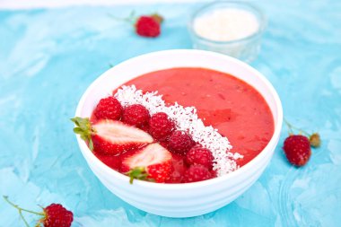 Güler yüzlü kase. Mavi arka plan üzerinde sağlıklı kahvaltı kase. Çilek ve Hindistan cevizi ile ahududu güler yüzlü. Vegan gıda