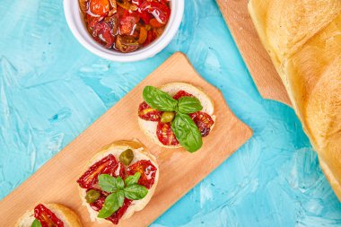 Bruschetta veya crostini ile güneş domates ve mavi arka plan ile bir ahşap mutfak tahtada Kapari kurumuş. Taze İtalyan sandviç. Lezzetli aperatif ve meze. Meze. Teras yatıyordu. Uzay kopyalayın. üstten görünüm. 