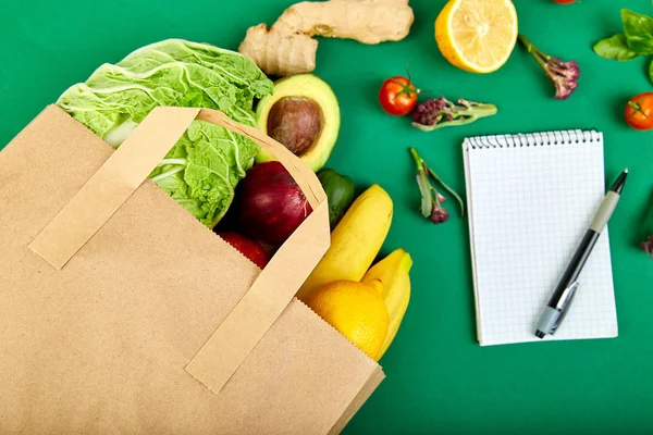 Shopping list, recipe book, diet plan. Grocering concept. Full paper bag of different fruits and vegetables,  ingredients for healthy cooking on a color background. healthy food.  Diet or vegan food, vegetarian. Top view. Flat lay.