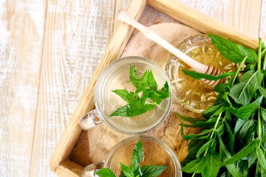 Cam bardak veya kupa ahşap tepsi üzerinde sıcak bitkisel Nane çay içecek. Bal ve taze Bahçe Nane yaprakları kopya alanı. Üstten görünüm.