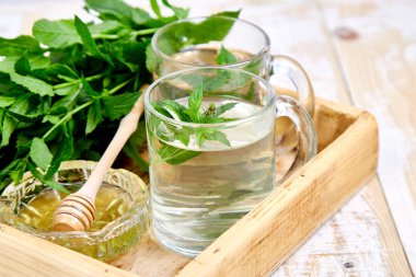 Cam bardak veya kupa ahşap tepsi üzerinde sıcak bitkisel Nane çay içecek. Bal ve taze Bahçe Nane yaprakları kopya alanı. 