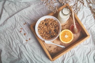 Günaydın. Beyaz çarşaf üzerinde Odaya Servis Kahvaltı. Müsli veya granola, süt, portakal yukarıdan ahşap tepsi. Üstten görünüm. Düz yatıyordu. Uzay kopyalayın. Otel odasında sabah erken.