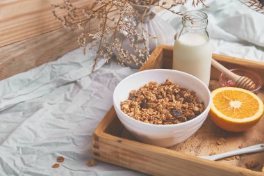 Günaydın. Beyaz çarşaf üzerinde Odaya Servis Kahvaltı. Müsli veya granola, süt, portakal yukarıdan ahşap tepsi. Üstten görünüm. Düz yatıyordu. Uzay kopyalayın. Otel odasında sabah erken.