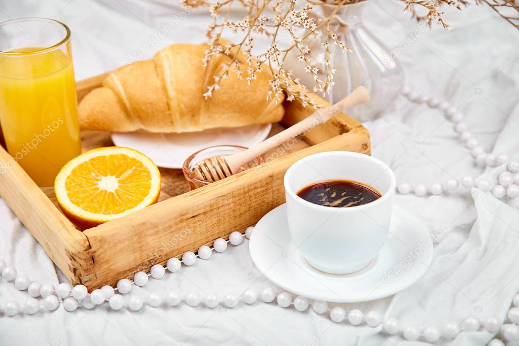 Good morning. Continental breakfast on white bed sheets. Cup of coffee, orange juice, croissants, jam on wooden tray from above. Top view.  Flat lay. Copy space. Hotel Room Early Morning 