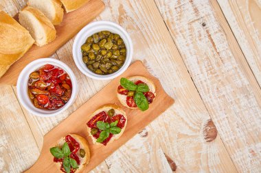 Bruschetta veya crostini ile güneş domates ve kapari ahşap mutfak tahtası ahşap arka plan ile kurutulmuş. Taze İtalyan sandviç. Lezzetli aperatif ve meze. Meze. Teras yatıyordu. Uzay kopyalayın. üstten görünüm. 