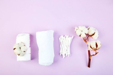 Pamuk bitki, kulaklı sopa, Pamuklu ped, havlu, kozmetik makyaj çıkarıcı tampon, hijyenik hijyenik temizleme bezi mor arka plan üstten görünüm üzerinde Şubesi. Spa kavramı. Düz yatıyordu. Kopya alanı.