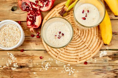 Yulaf ya da yulaf ezmesi, muz ve ahşap rustik zemin üzerine nar ile güler yüzlü. Sağlıklı içecek kahvaltı. Protein diyet milkshake. Üstten görünüm. Kopya alanı.
