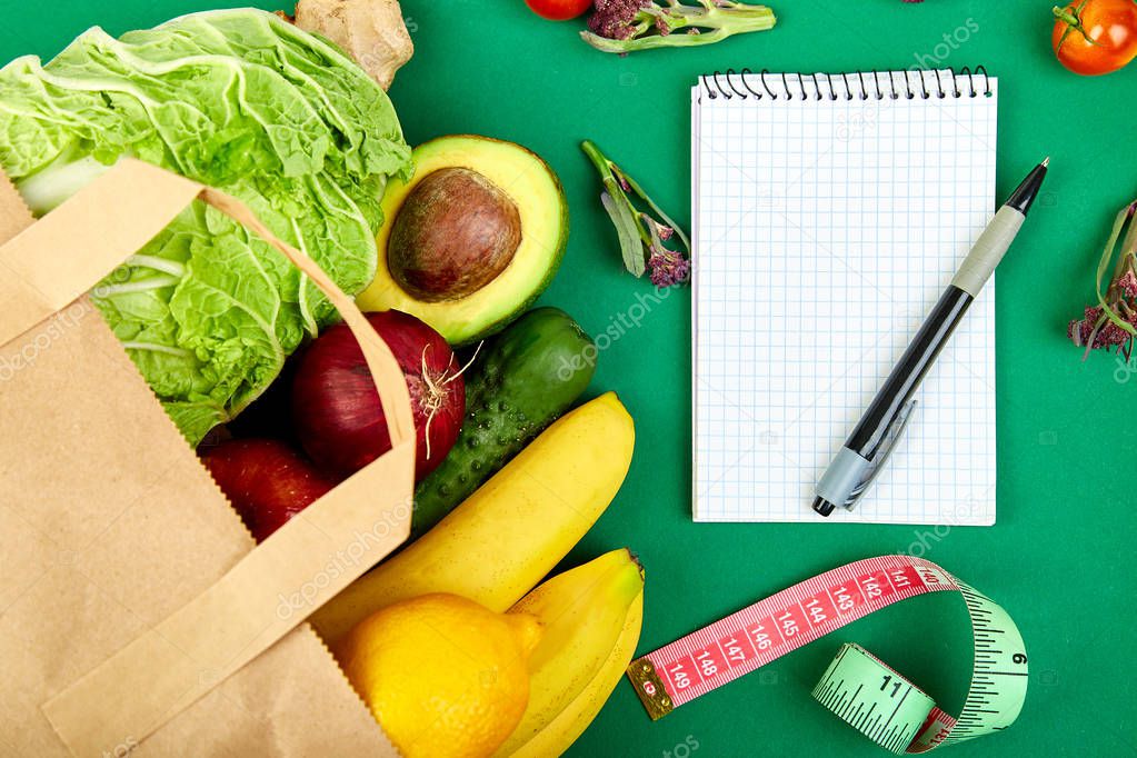 Shopping list, recipe book, diet plan. Grocering concept. Full paper bag of different fruits and vegetables,  ingredients for healthy cooking on a color background. healthy food.  Diet or vegan food, vegetarian. Top view. Flat lay. 