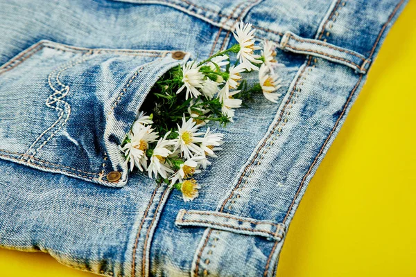 黄色背景的牛仔裤口袋里的白色花的花束 最小的 粗斜纹棉布概念 平躺着 复制空间 春季节日主题的创意布局 — 图库照片