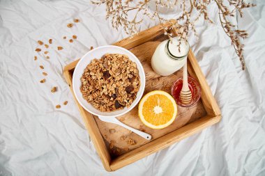 Günaydın. Beyaz çarşaf üzerinde Odaya Servis Kahvaltı. Müsli veya granola, süt, portakal yukarıdan ahşap tepsi. Üstten görünüm. Düz yatıyordu. Uzay kopyalayın. Otel odasında sabah erken.