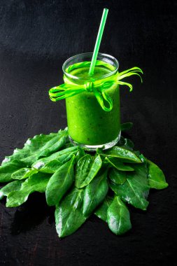 Ispanak güler yüzlü. Siyah masada malzemelerle karışık yeşil smoothie. Sağlıklı, vegan, diyet. Detoks