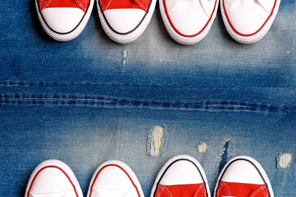 White and red sneakers on a the ripped denim background. Casual style items of men top view with copy space. Flat lay