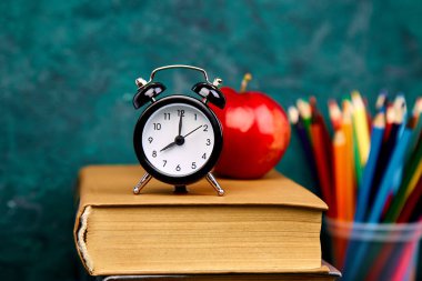Okula dönüş sağlar. Kitap ve yeşil zemin üzerine kırmızı elma. Çalar saat ile natürmort. Kopya alanı.