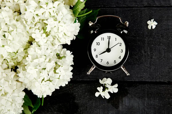 黑色的闹钟和白色的花朵在黑色的背景 母亲或妇女日 早上好早餐 顶部视图 复制空间 — 图库照片