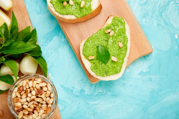 Bruschetta ekmek pesto sos, parmesan peyniri ve taze fesleğen ile mavi arka plan üzerinde bırakır. Abur cubur. Meze. Crostini. İtalyan yemeği. Üstten görünüm. Düz yatıyordu. Kopya alanı.