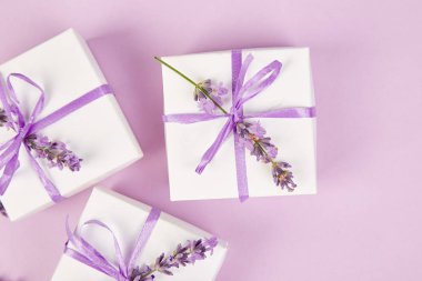Mor Şerit ve buket çiçek lavanta pembe bir arka plan üzerinde beyaz hediye kutusu. Kutlama, Doğum günü. Dekorasyon mevcut. Düz yatıyordu. Kopya alanı.