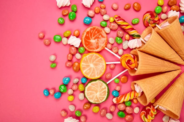 Renkli şekerli dondurma külahları, tatlı jölesi, çubukta lolipop, pembe arka planda çok renkli şekerlerin serpilmesi. Üst Manzara 'da dümdüz yatıyordu. Boşluğu kopyala.