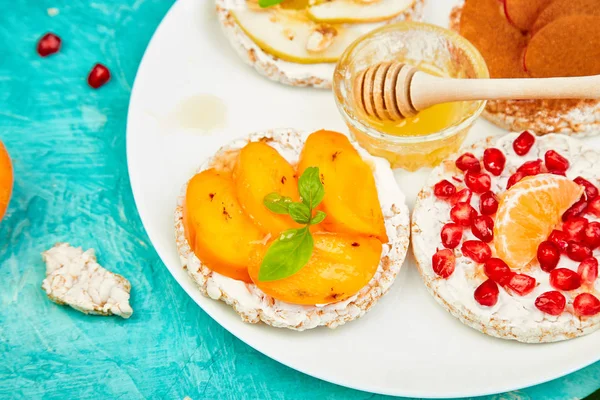 Rice Crisp bread healthy snack with tropical fruit - pomegranate, tangerine, persimmon, apple. Easy breakfast close-up on a blue background. Summer vegan, diet, organic natural food. Copy space. Flat lay. Top view