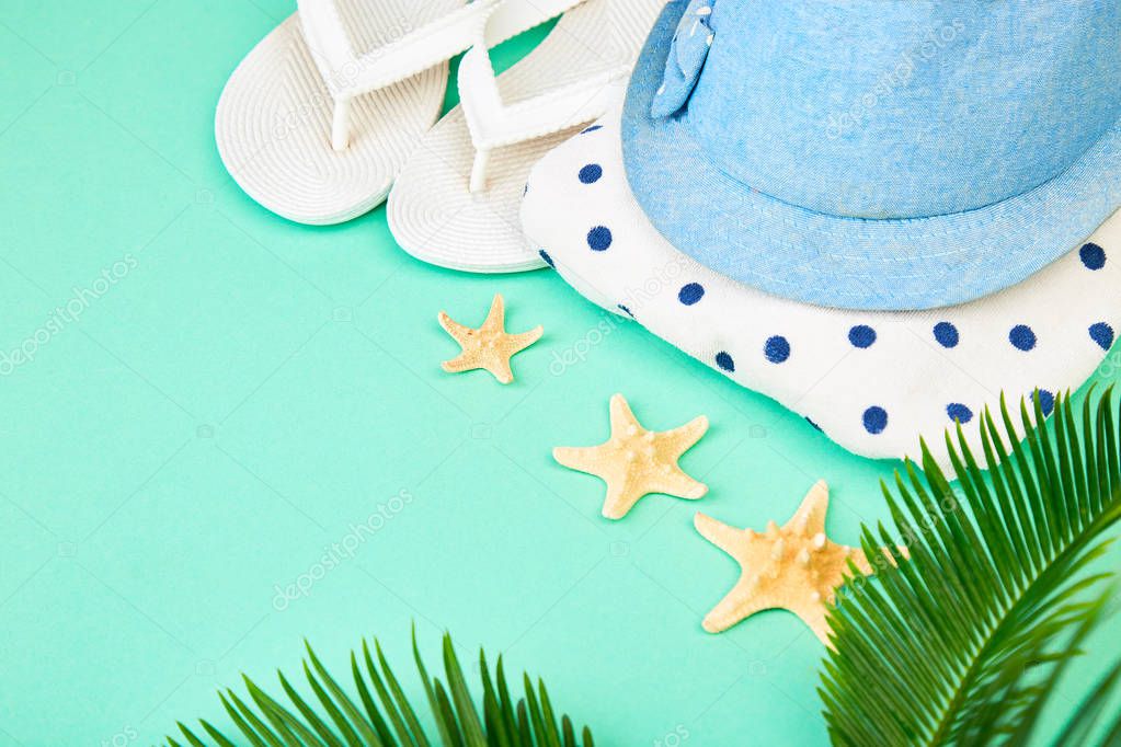 Summer female fashion outfit. Sunhat, white flip flops, polka dot towel, and starfish with tropical palm branches on blue background. Beach, vacation, travel concept, Minimalism.  Flat lay, top view. Copy space.