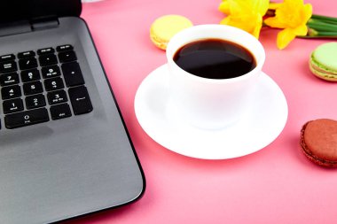 Kadın ya da laptop, defter, fincan kahve, macarons ve çiçekler nergis pembe tablo ile kadınsı çalışma alanı. Üstten görünüm. Düz yatıyordu. Kopya alanı.