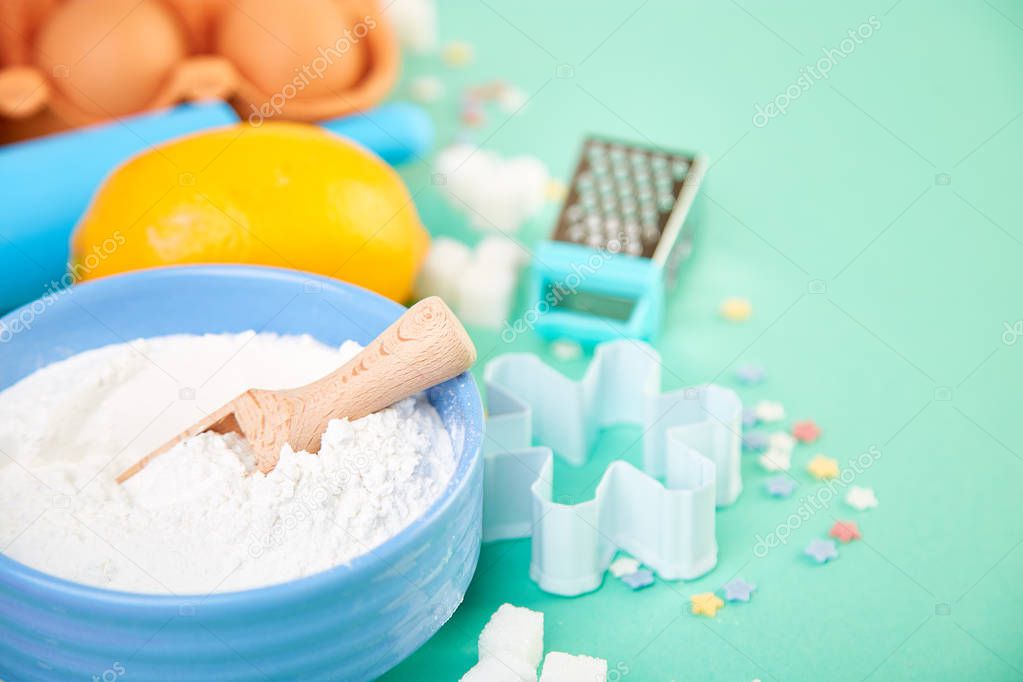 Baking or cooking ingredients - flour, eggs, lemon,  sugar, wooden spoon, rolling pin and different tools on a blue table background.  Dessert ingredients and utensils.  Bakery frame. Top view, copy space. Flat lay.