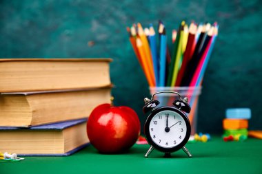 Okula dönüş sağlar. Kitap ve yeşil zemin üzerine kırmızı elma. Çalar saat ile natürmort. Kopya alanı.