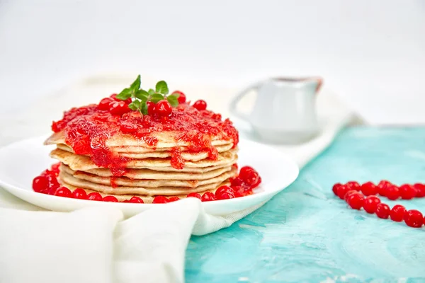 American pancake with jam - berry, viburnum, cranberry on blue background. Homemade pancakes with berry sauce and mint. Healthy breakfast with fresh hot pancakes with berry jam