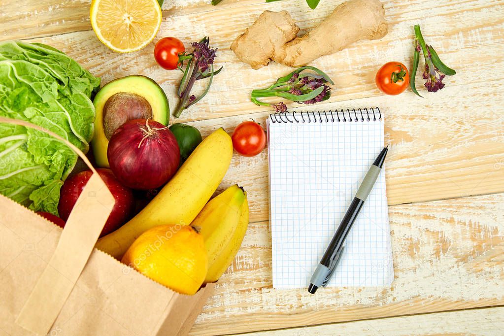 Shopping list, recipe book, diet plan. Grocering concept. Full paper bag of different fruits and vegetables,  ingredients for healthy cooking on a wooden background. healthy food.  Diet or vegan food, vegetarian. Top view. Flat lay. 