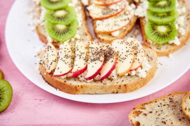 Sağlıklı kahvaltı tost kivi, elma, peynir ve chia tohum beyaz plaka ve pembe bir arka plan ile. Yakın çekim. Diyet yemekleri. Vegan.