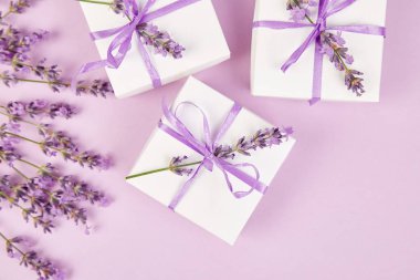 Mor Şerit ve buket çiçek lavanta pembe bir arka plan üzerinde beyaz hediye kutusu. Kutlama, Doğum günü. Dekorasyon mevcut. Düz yatıyordu. Kopya alanı.