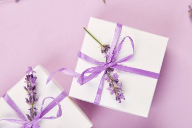 Mor Şerit ve buket çiçek lavanta pembe bir arka plan üzerinde beyaz hediye kutusu. Kutlama, Doğum günü. Dekorasyon mevcut. Düz yatıyordu. Kopya alanı.