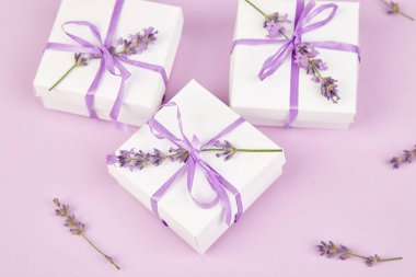 Mor Şerit ve buket çiçek lavanta pembe bir arka plan üzerinde beyaz hediye kutusu. Kutlama, Doğum günü. Dekorasyon mevcut. Düz yatıyordu. Kopya alanı.