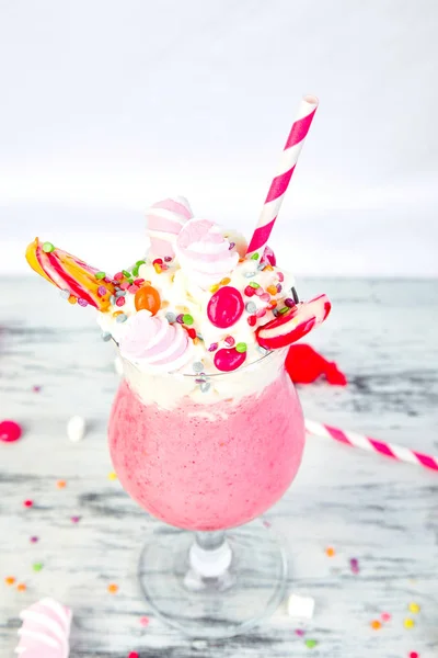 Pink Extreme milkshake with berry, rasberry, strawberry, candy marshmallow, lollipops on white background. Crazy freakshake. Copy space. Food trend. Overshake
