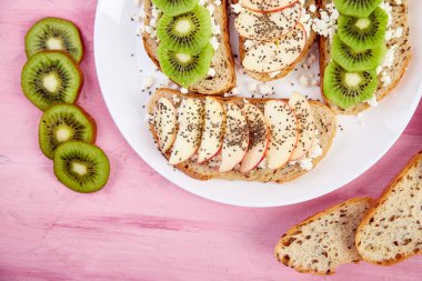 Sağlıklı kahvaltı tost kivi, elma, peynir ve chia tohum beyaz plaka ve pembe bir arka plan ile. Üstten Görünüm, düz yatıyordu. Diyet yemekleri. Vegan.