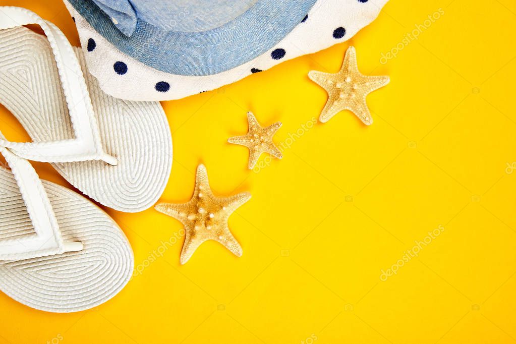 Colorful summer female fashion outfit. Sunhat, white flip flops, polka dot towel, and starfish on yellow background. Beach, vacation, travel concept, Minimalism. Flat lay, top view. Copy space