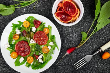 Roka feta, Chia, Kumquat ve siyah arka planda kan portakal ile taze narenciye salatası. Vegan, Vejetaryen, temiz yemek, diyet, gıda konsepti. Üst görünüm, düz yatıyordu, kopya alanı