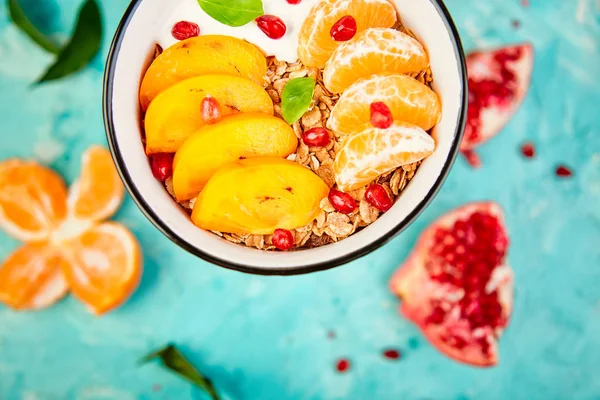 Tropical  smoothies bowl  fruit Breakfast homemade granola yogurt pomegranate, tangerine, persimmon on blue background. healthy organic layered dessert. Diet, vegan food. Top View