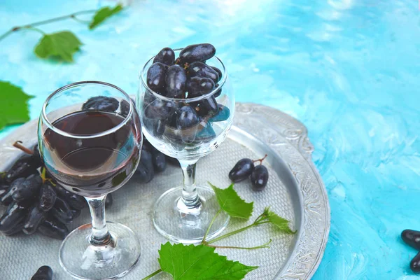 Red wine concept with bottle, glass and grapes on silver tray on blue background, copy space. Wine header image. Wineglasses