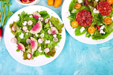 Mavi arka planda salataları karıştırın. Arugula feta, chia, kumquat ve kan portakal ile Taze Narenciye Salatası. Karpuz turp salatası. Vegan, vejetaryen, temiz beslenme, diyet, gıda konsepti. Üst görünüm, düz döşeme, kopyalama alanı