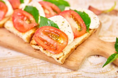 Caprese bruschetta bir kesme tahtası üzerinde tost. Bruschetta domates, mozzarella peyniri ve fesleğen rustik bir masada. Geleneksel İtalyan meze veya aperatif, antipasto